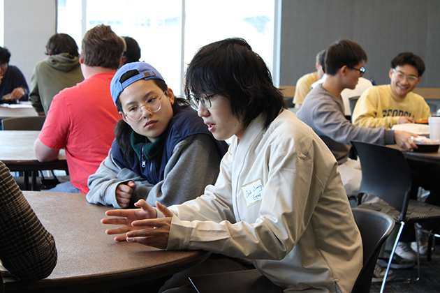 two students sitting at desks and talking