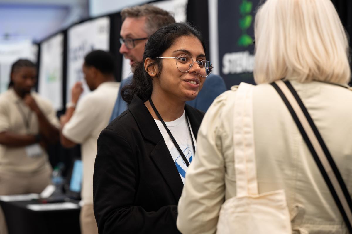 Two attendees engage in conversation during a Georgia Tech innovation showcase, with others networking in the background.